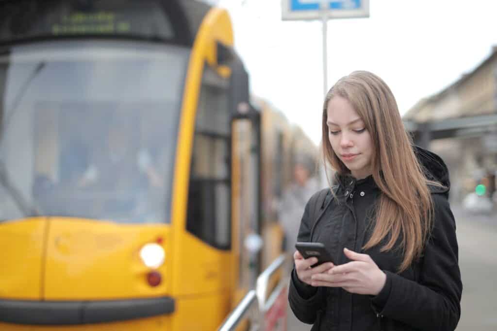 Woman in Black Jacket Standing Beside Yellow Tram