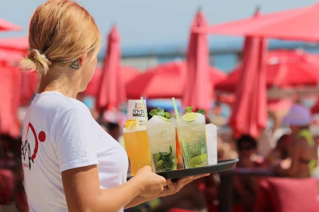 A cocktail server carrying drinks in a casino with tip money on the tray.