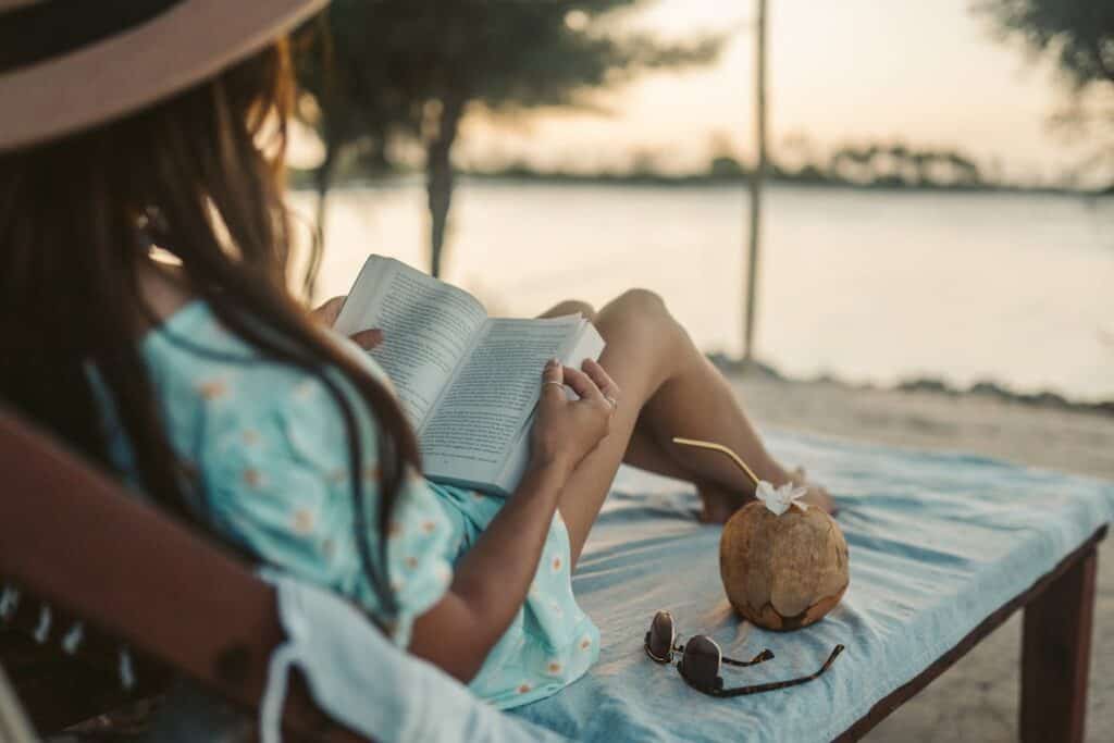 A traveler writing or reading on a balcony overlooking a quiet village or coastal town at sunset.