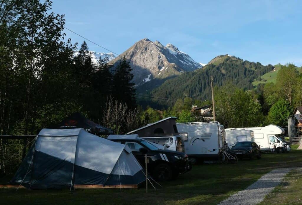An RV moving slowly past tents and families.