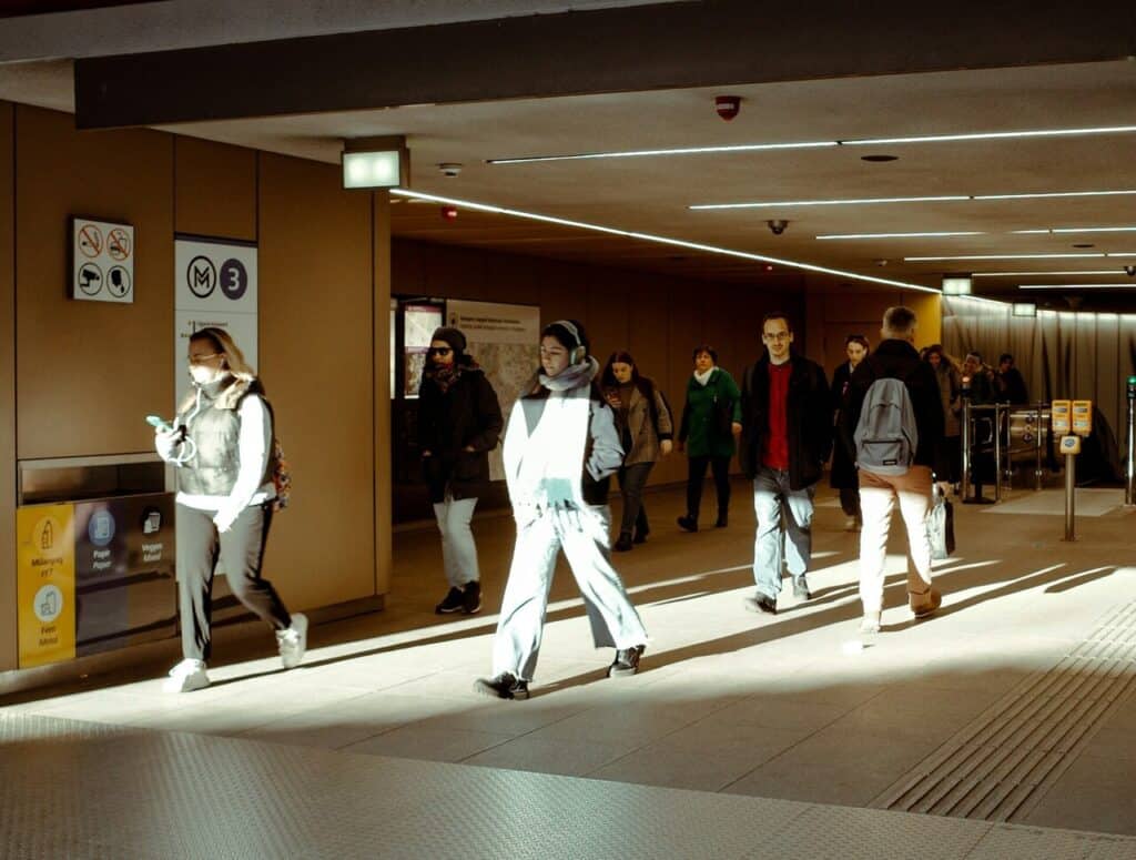 A clean, modern metro or tram station with commuters carrying backpacks.