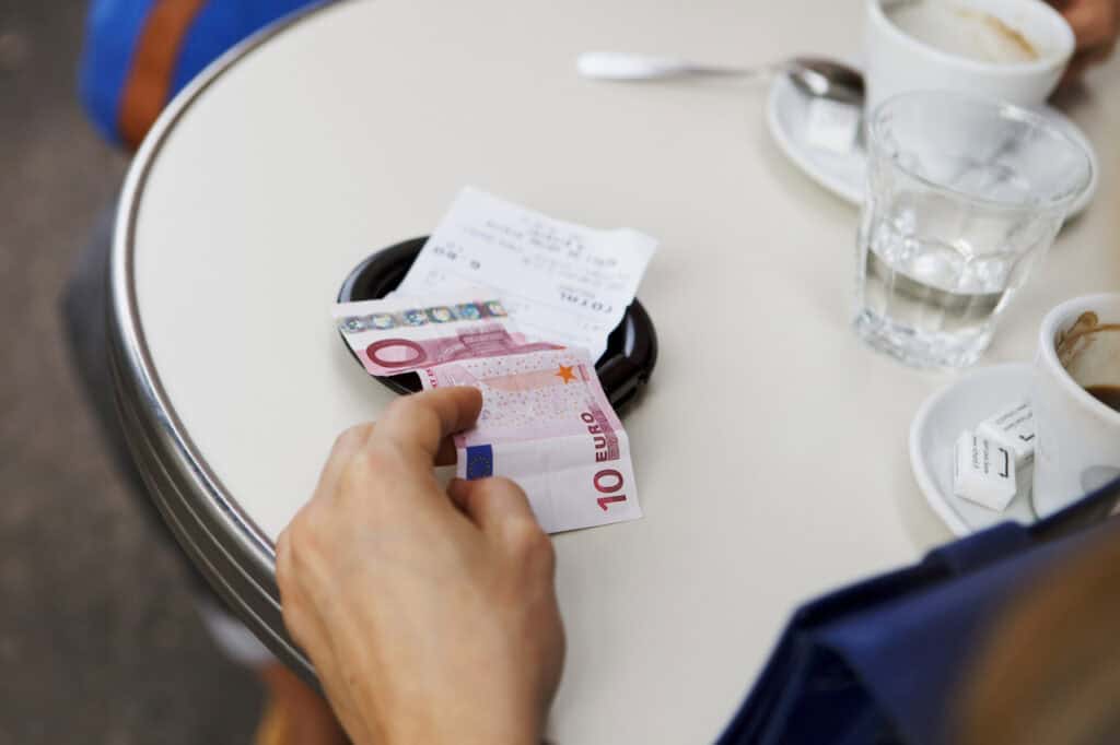 Hand leaving a tip beside a restaurant check or coffee cup.