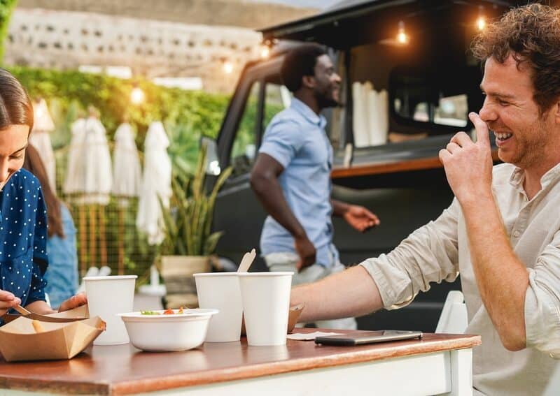 Young people having fun eating at food truck restaurant outdoor - Focus on right man face