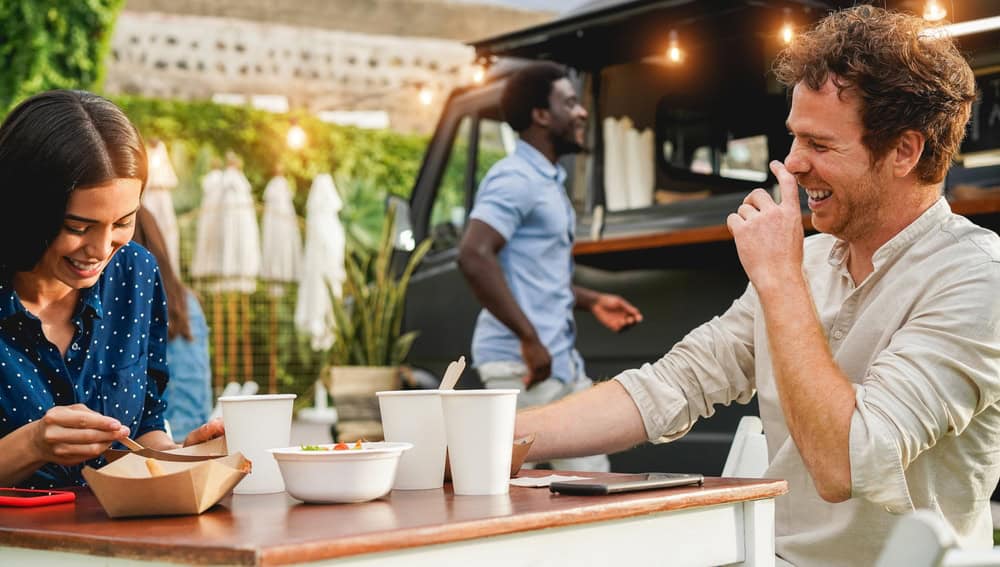 Young people having fun eating at food truck restaurant outdoor - Focus on right man face