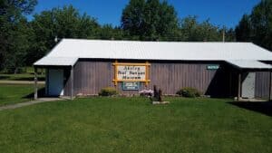 Akeley Paul Bunyan Museum building in a green park with clear blue sky, visitors information sign outside.