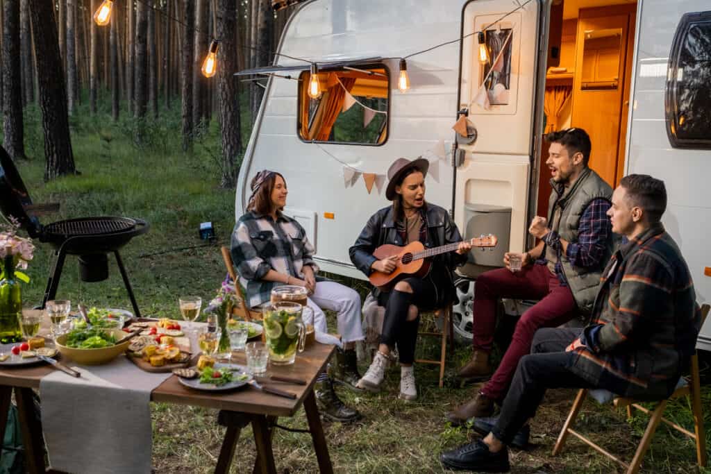 Side view of multi-ethnic friends group standing in raw on sand while they are looking away ocean against a camper van in background
