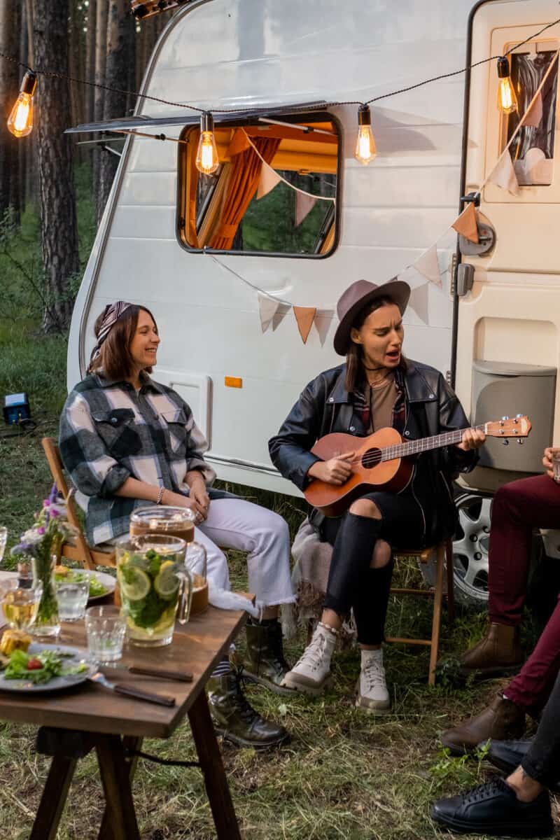 Side view of multi-ethnic friends group standing in raw on sand while they are looking away ocean against a camper van in background