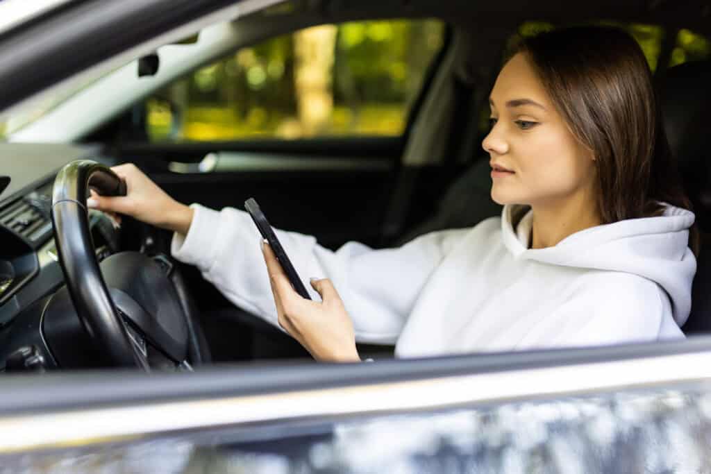 Young woman checking smartphone while sitting in car, enjoying travel and road trip.