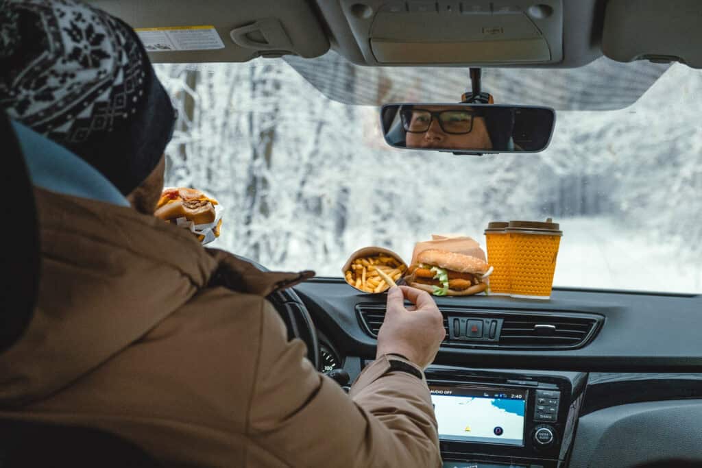 winter road trip happy man eats while driving car.