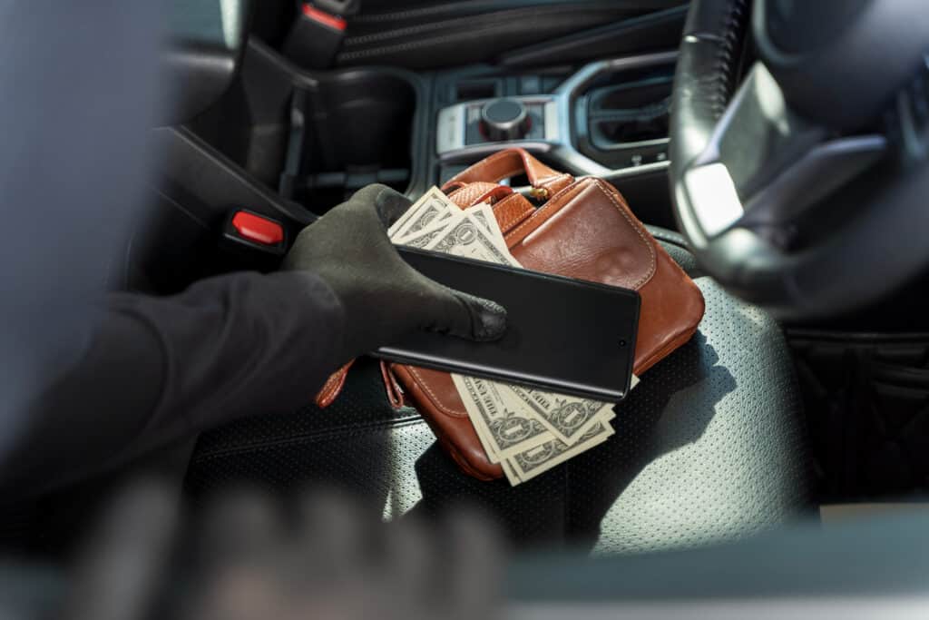 Thief stealing phone and money from purse on car seat, concept o