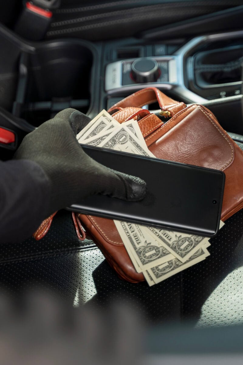 Thief stealing phone and money from purse on car seat, concept o