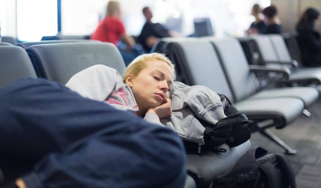 Tired female traveler sleeping on the airpot departure gates bench with all her luggage by her side.