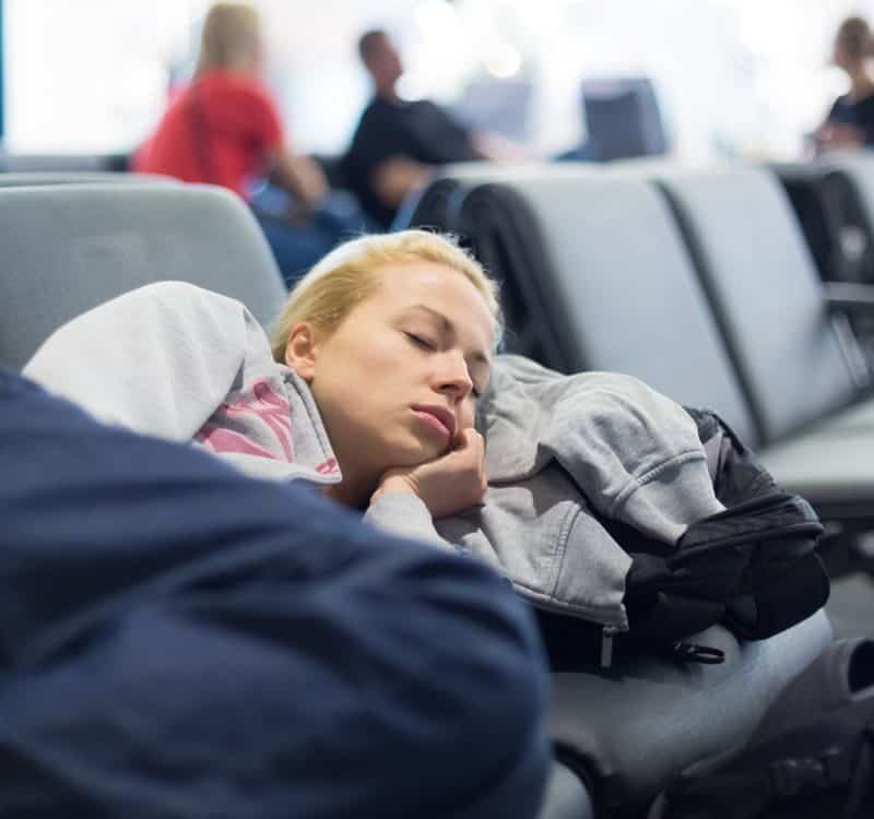 Tired female traveler sleeping on the airpot departure gates bench with all her luggage by her side.
