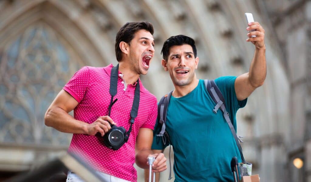 Two cheerful positive smiling friends are walking with baggage and making selfie in Barcelona.