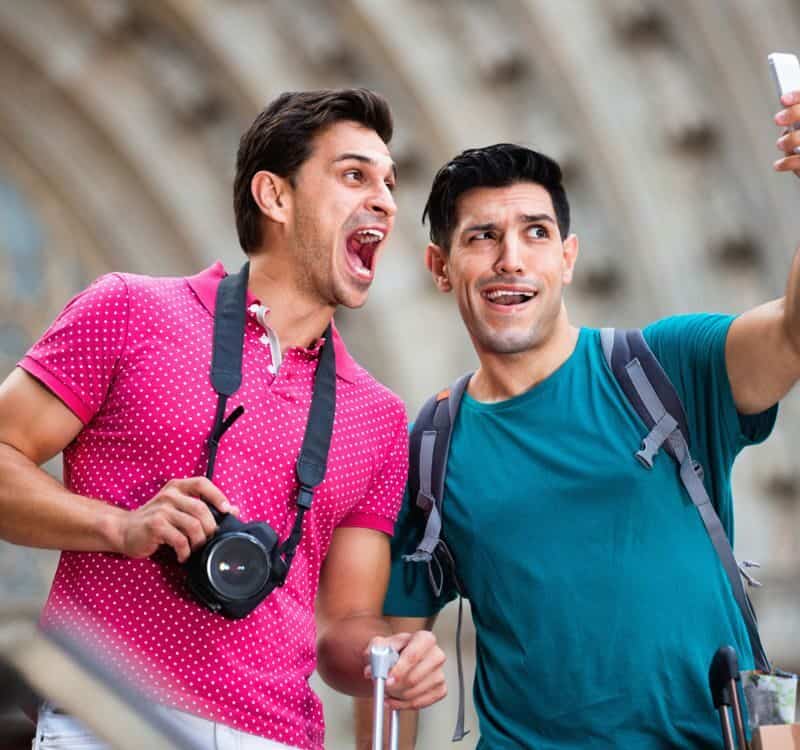 Two cheerful positive smiling friends are walking with baggage and making selfie in Barcelona.