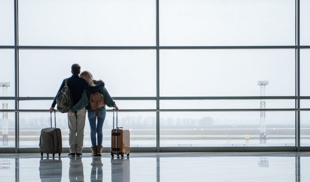 Two young people embracing while looking at the beautiful view from the airport window. Copy space in right side