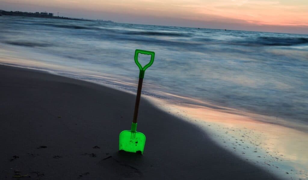 a green toy shovel stuck in the sand on the beach with the sea in the background photography of beaches
