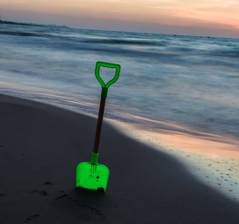 a green toy shovel stuck in the sand on the beach with the sea in the background photography of beaches