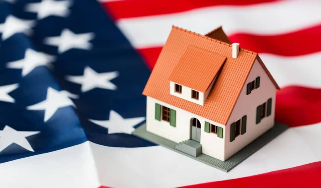 citizenship, residence, property, real estate and people concept - close up of living house model over american flag