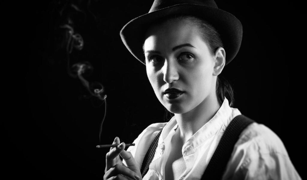 serious woman in hat smoking cigarette on black background, monochrome