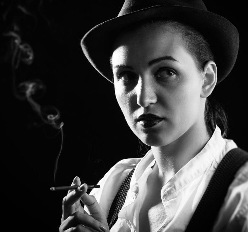serious woman in hat smoking cigarette on black background, monochrome