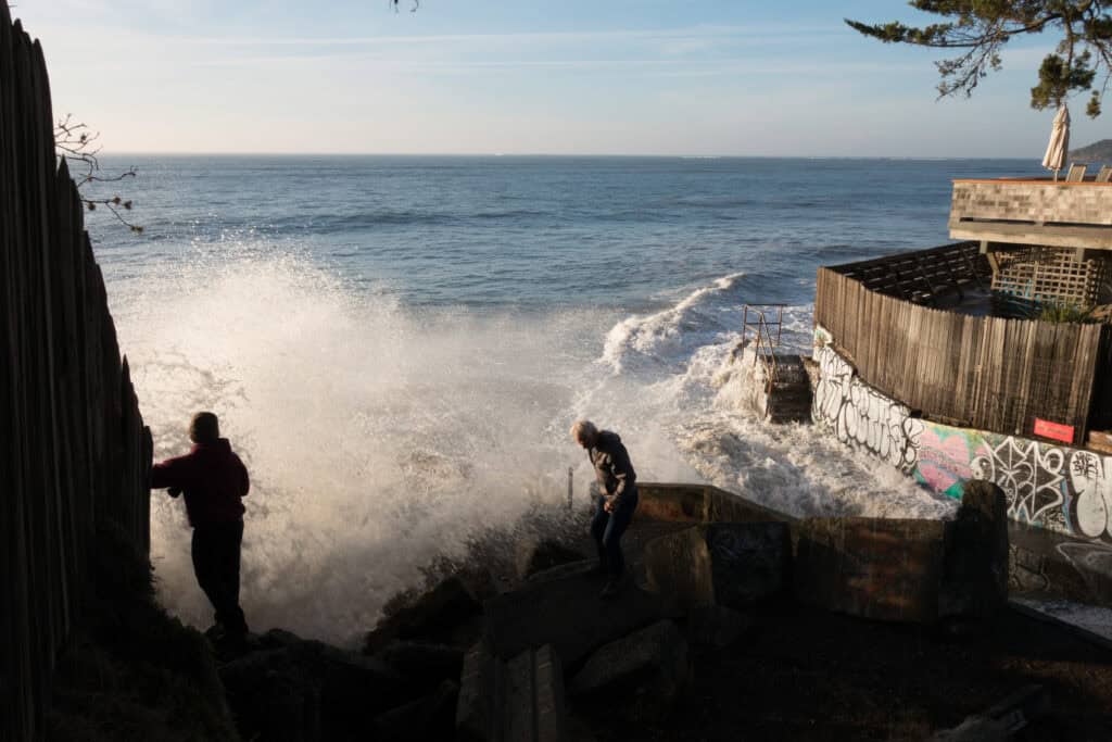 sneaker wave crashing on shore with tourists on black sand beach