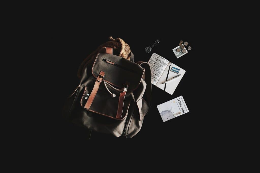 Backpack with travel organizer items including notebook, coins, and planner for travel planning.
