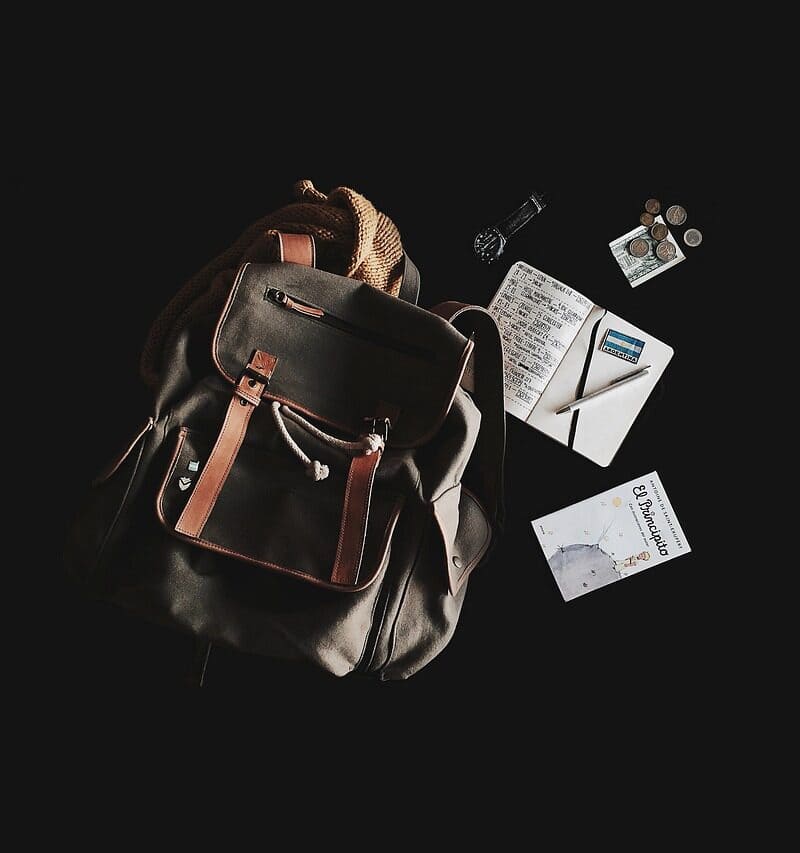 Backpack with travel organizer items including notebook, coins, and planner for travel planning.