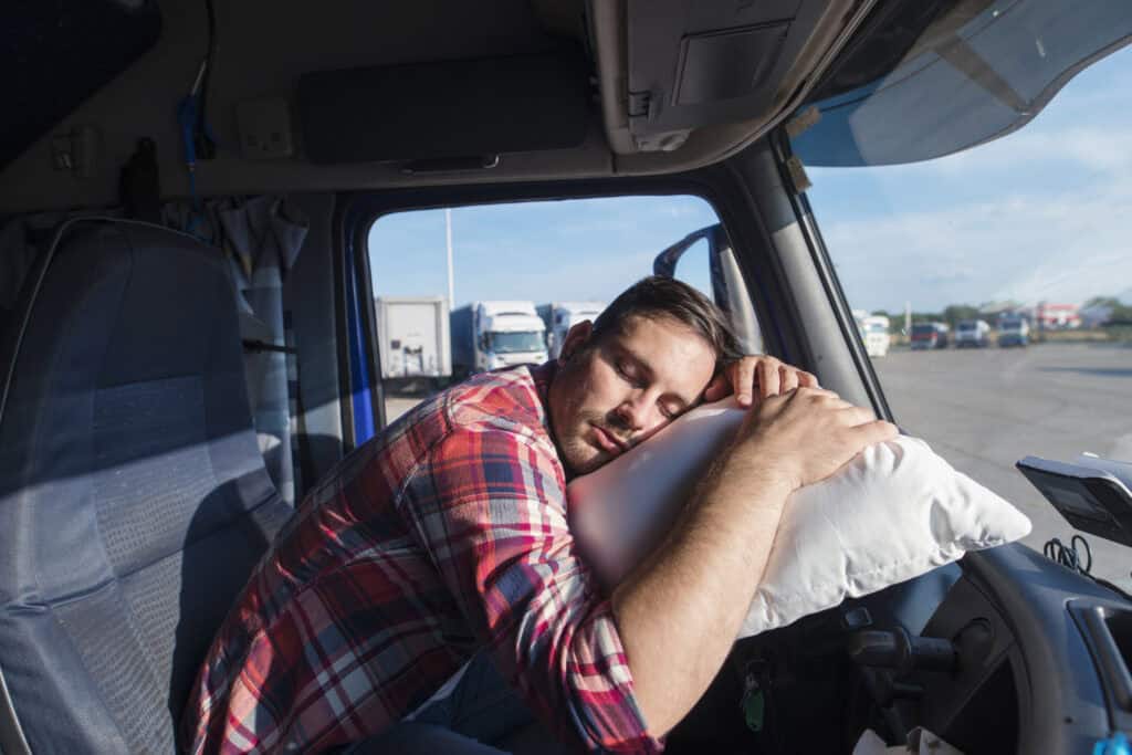  a man sleeping in car on steering wheel sleeping on his pillow.