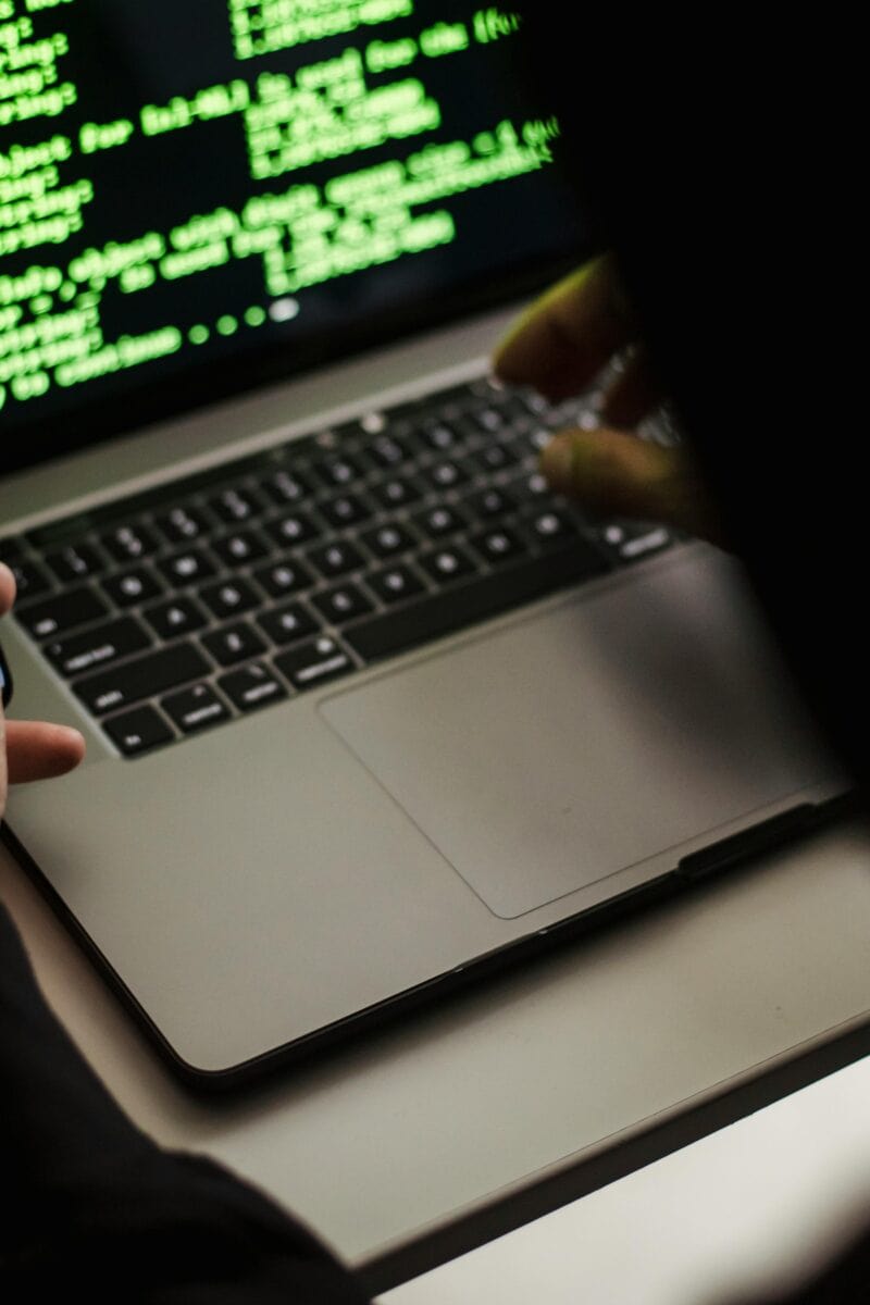 Crop unrecognizable developer using laptop and smartphone