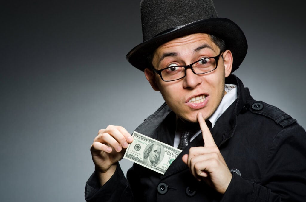 Young man in black coat holding money against gray