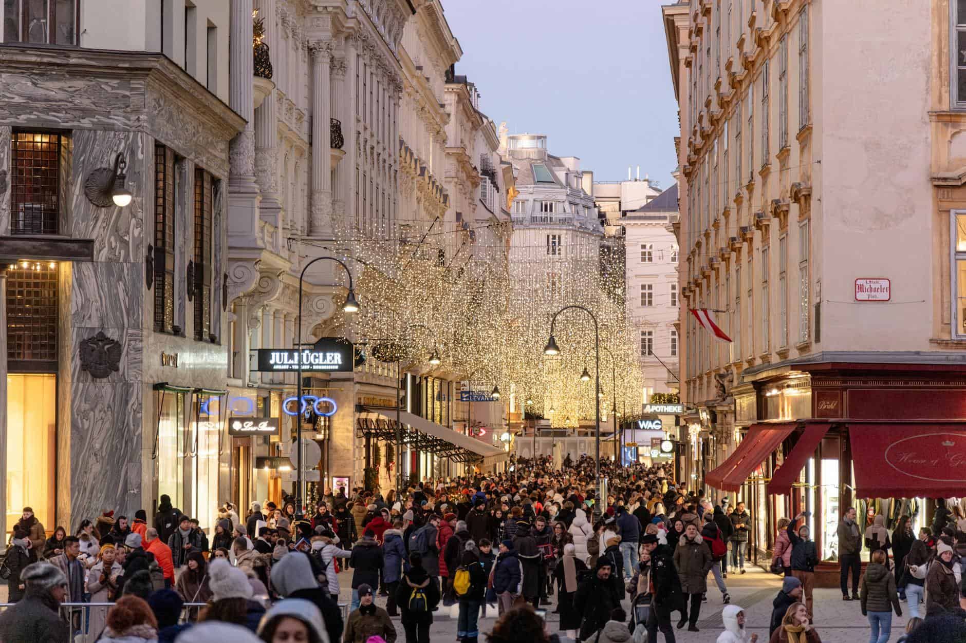 A bustling urban street in Vienna during the holiday season with festive lights and a vibrant crowd.