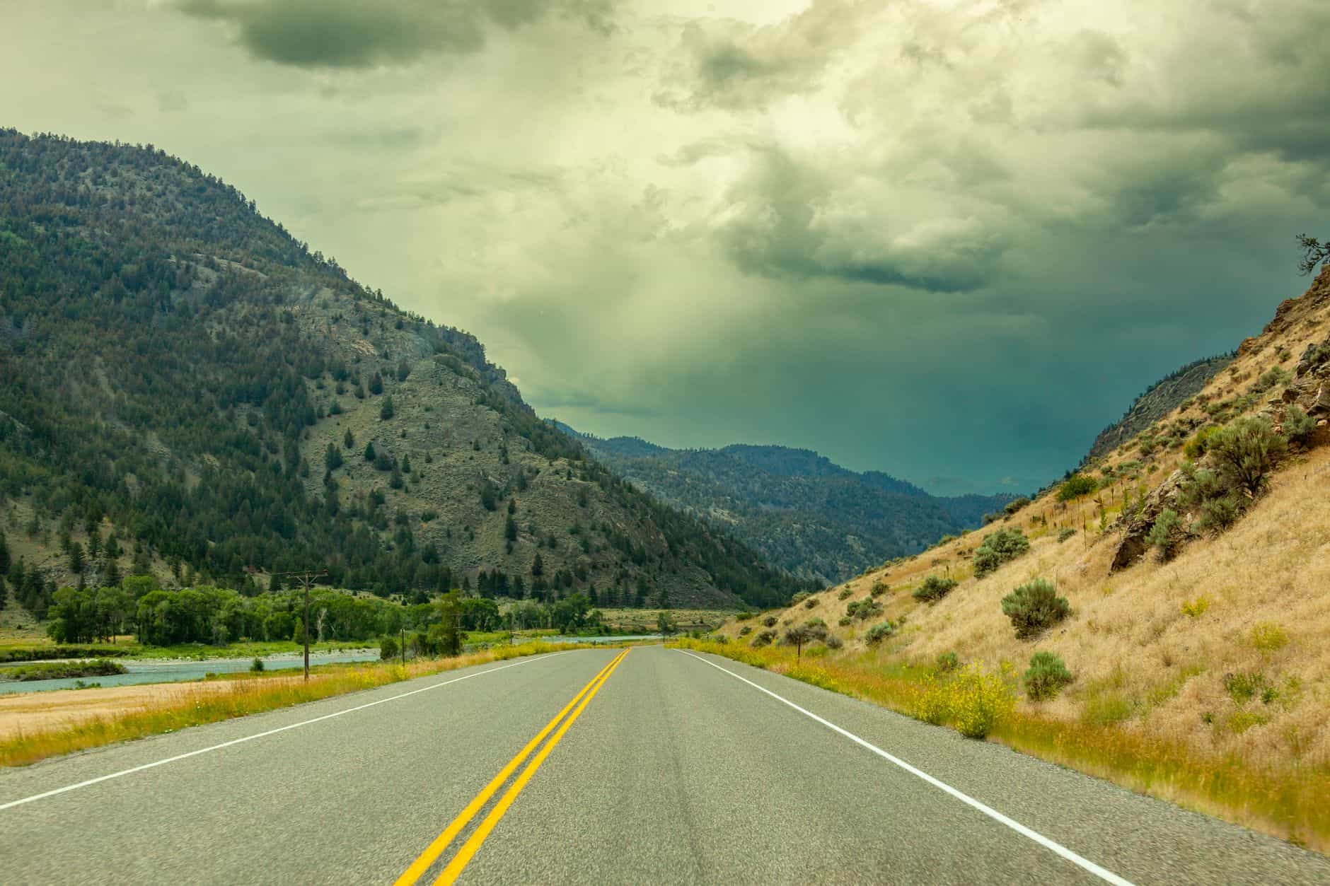 Scenic highway through Wyoming's mountainous countryside under dramatic cloudy skies.