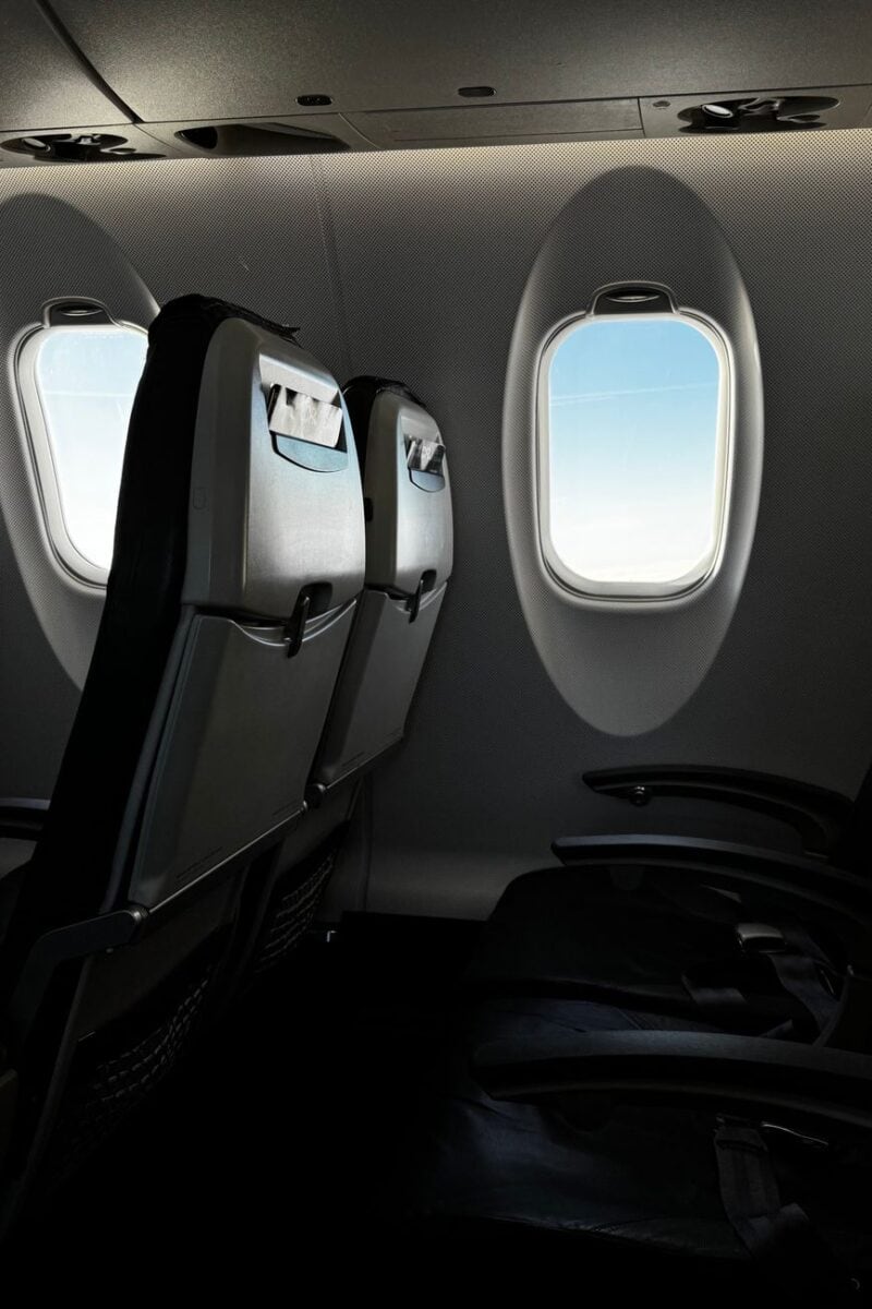 Interior of an empty airplane cabin with a bright sky visible through the window.