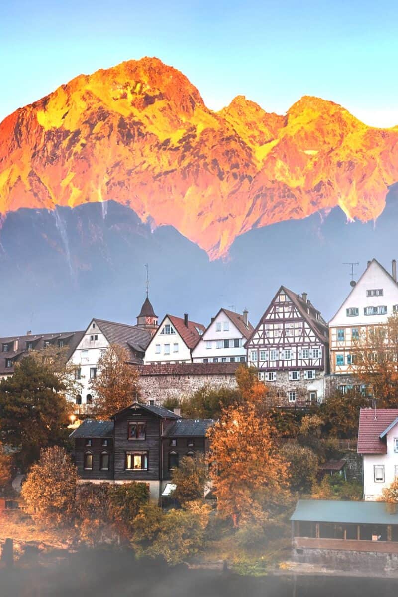 Picturesque European village with mountain backdrop at sunset, showcasing traditional architecture.