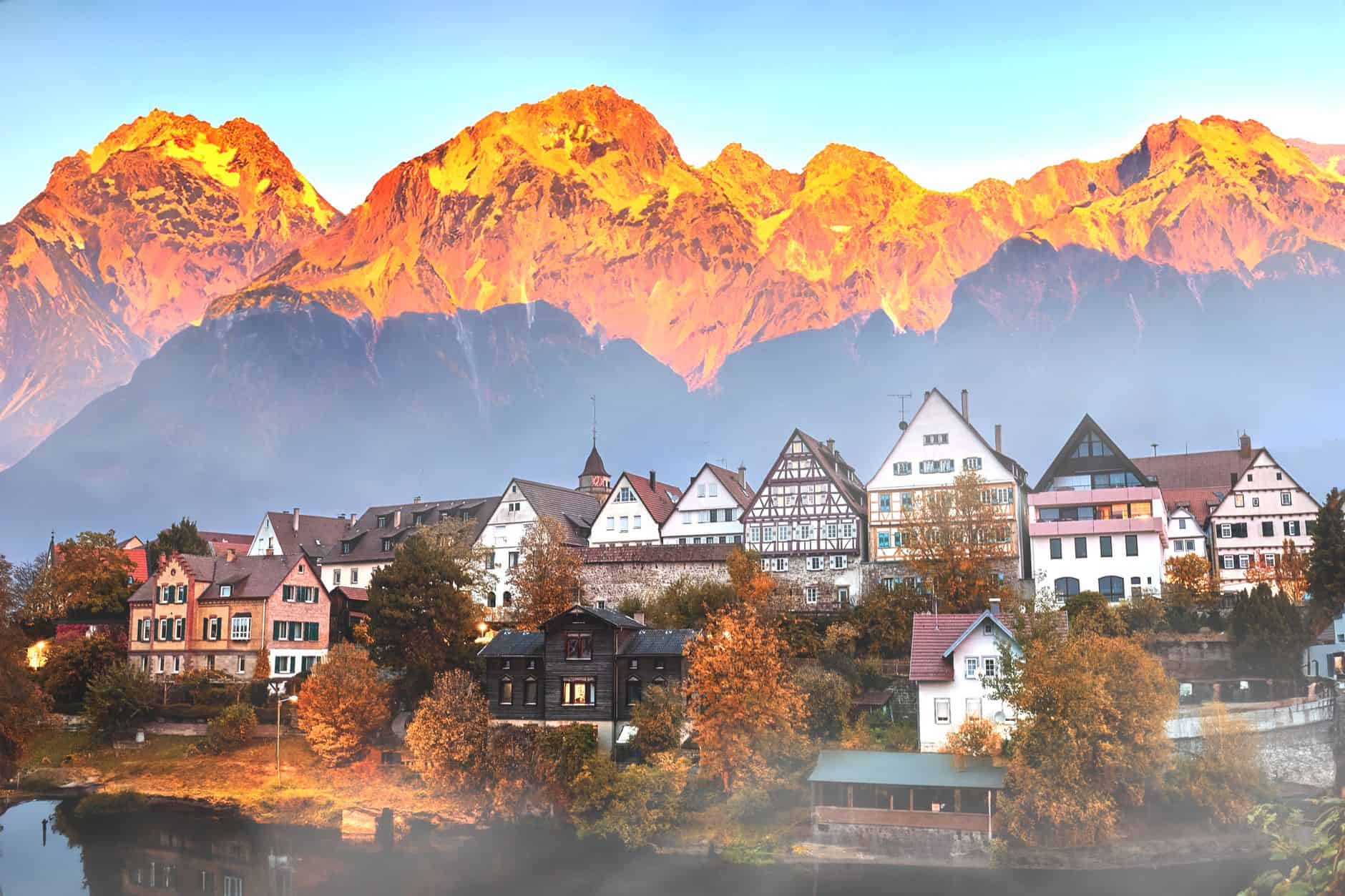 Picturesque European village with mountain backdrop at sunset, showcasing traditional architecture.