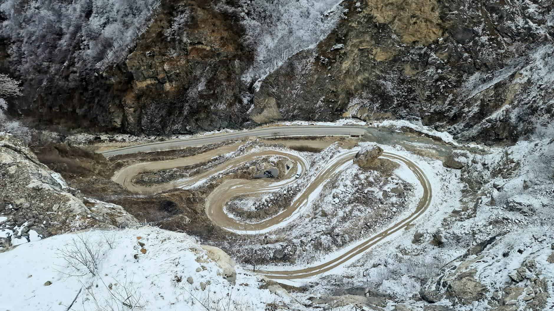 Aerial view of a snow-covered winding mountain road with scenic winter landscape.
