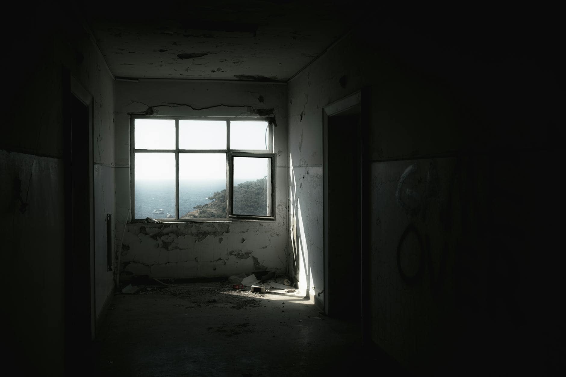 A dramatic view of the coast through a window in an abandoned building, conveying a sense of isolation and decay.