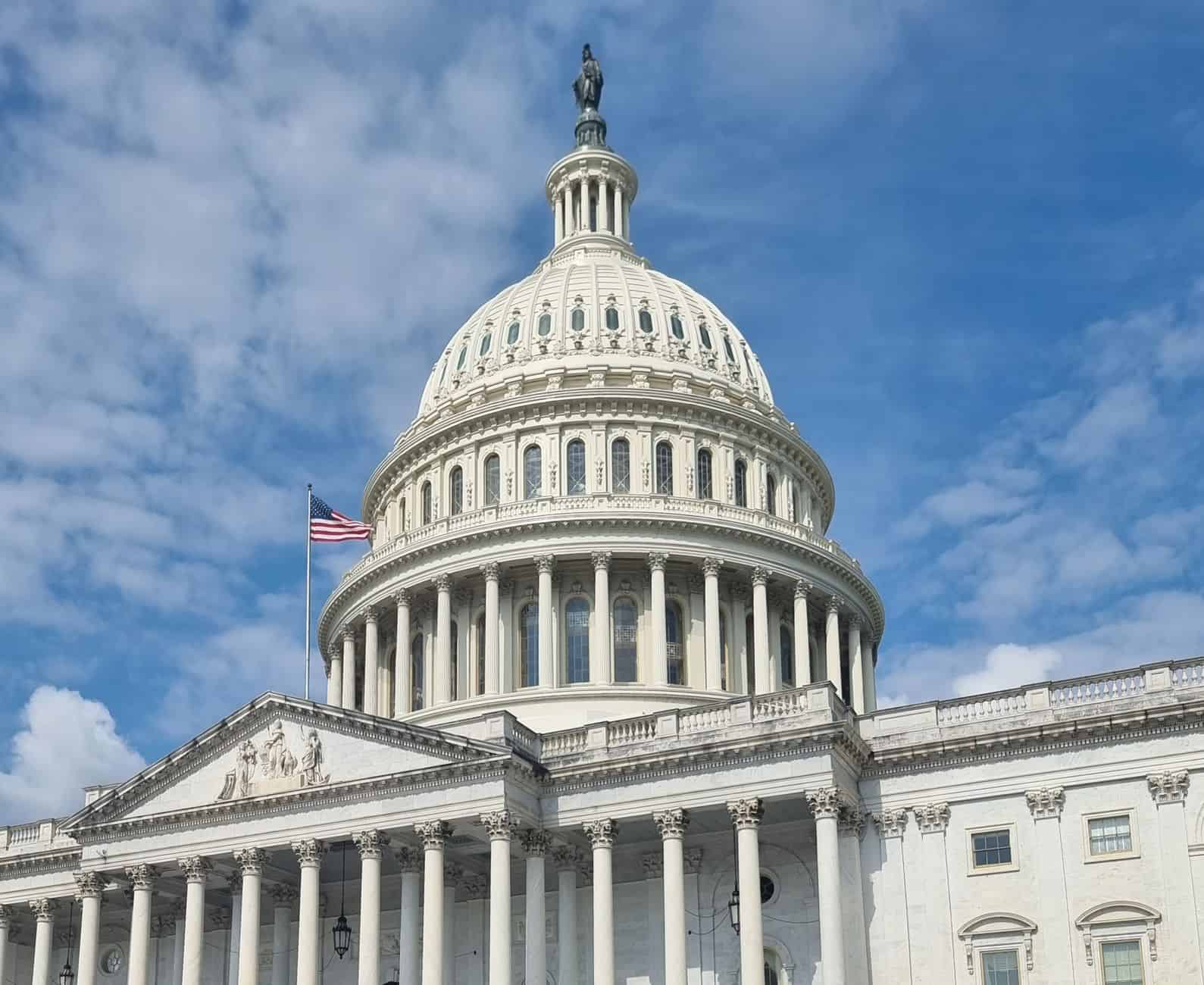 A striking view of the US Capitol dome with flag and blue sky in Washington, DC.