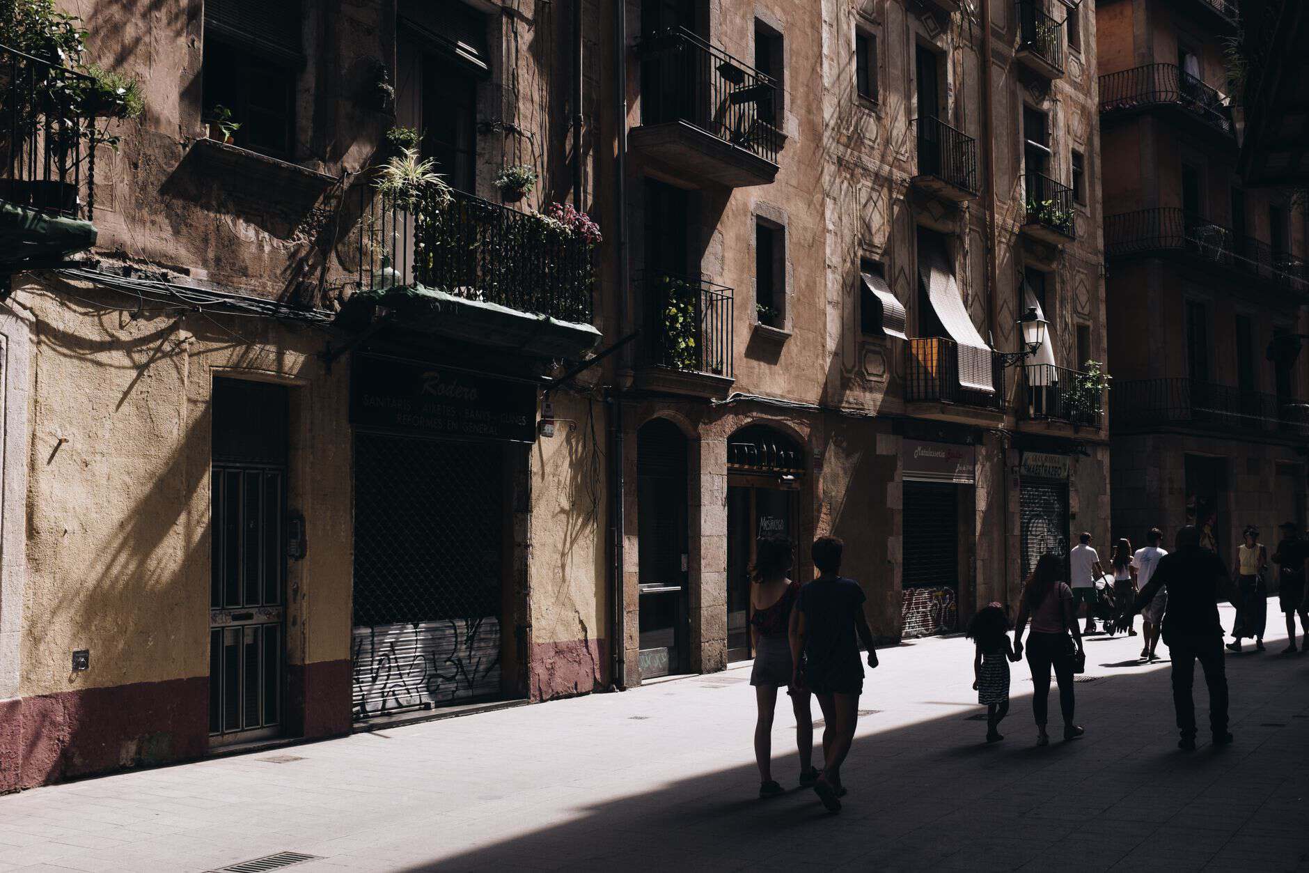 A bustling urban street in Barcelona with historical architecture and shadow play on the facades.