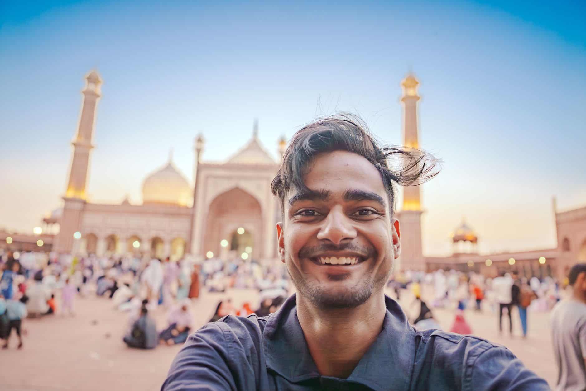 A smiling tourist takes a selfie at Jama Masjid in Old Delhi during sunset, showcasing Mughal architecture.
