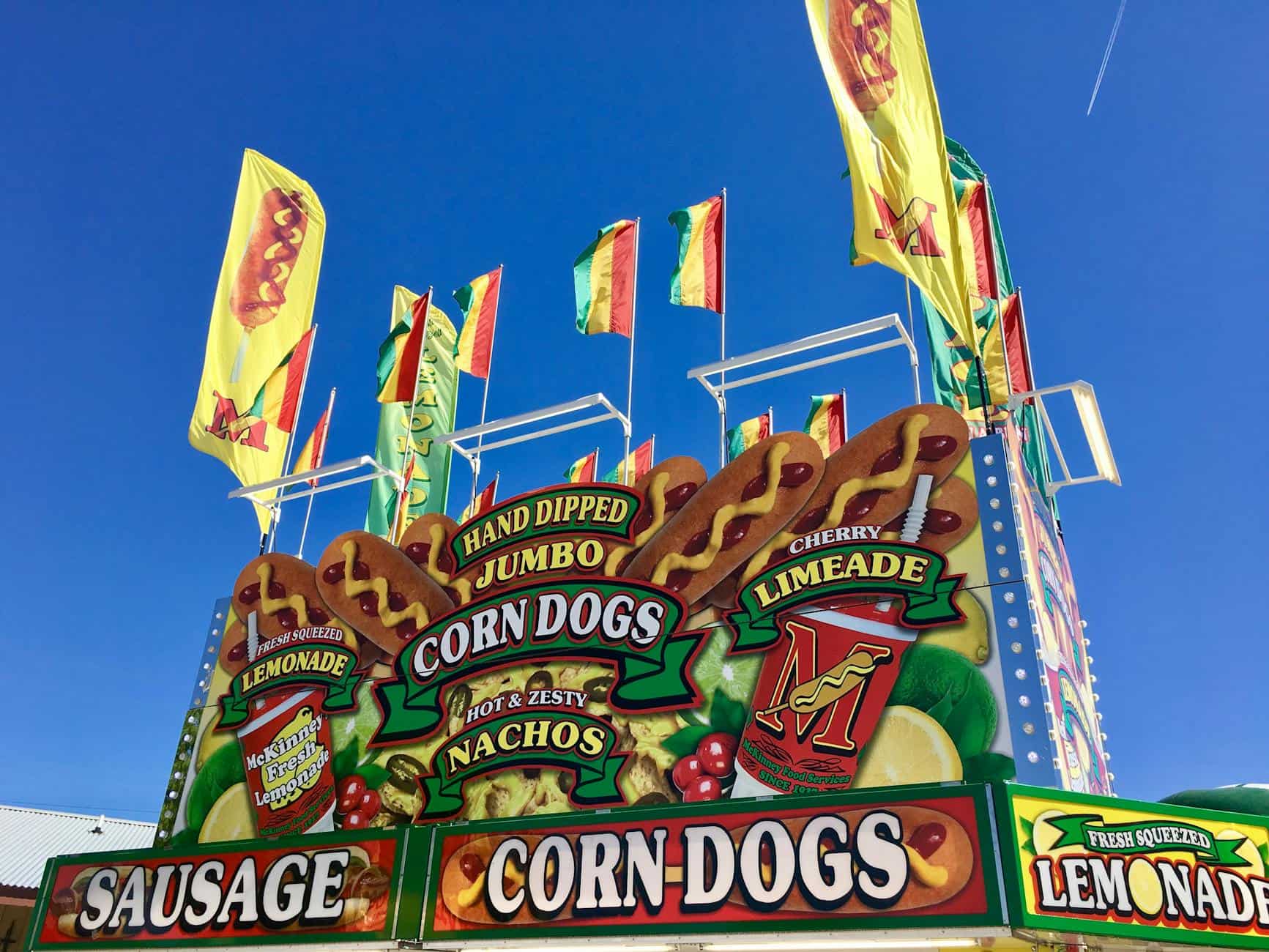 Vibrant fair stand in Grapevine, TX with corn dogs, lemonade, and flags under clear skies.