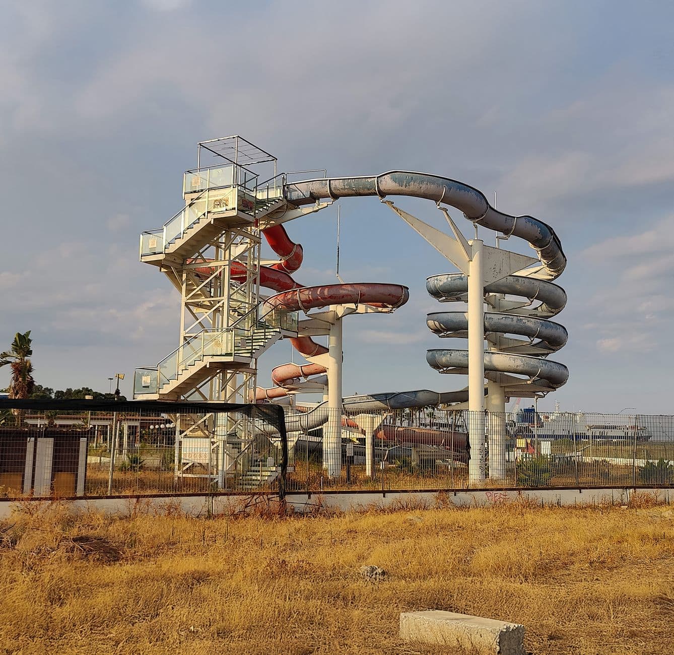 A rusting, abandoned water slide in Catania, Sicily, under a clear sky.