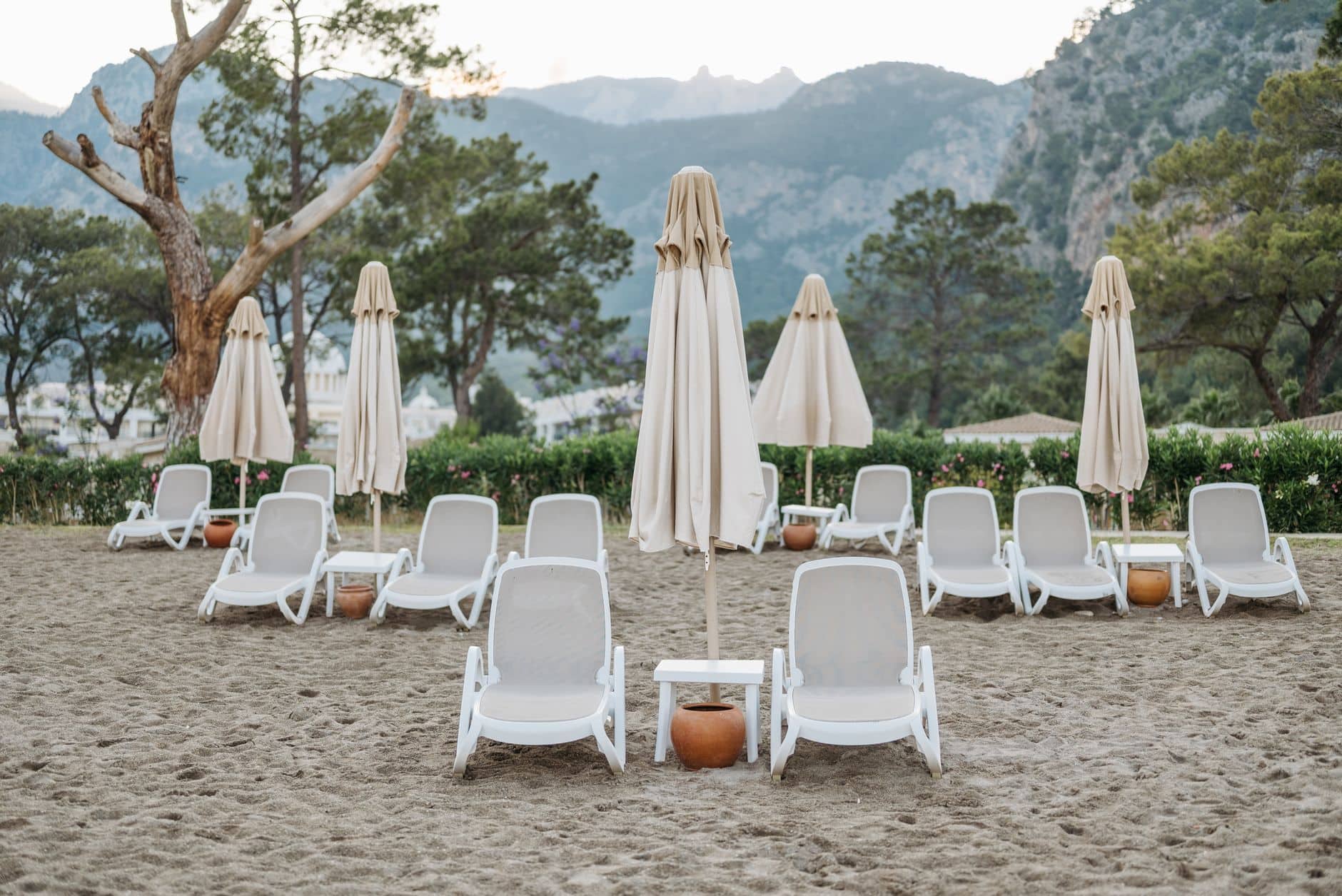 Tranquil beach scene with empty sunloungers and umbrellas surrounded by mountains.