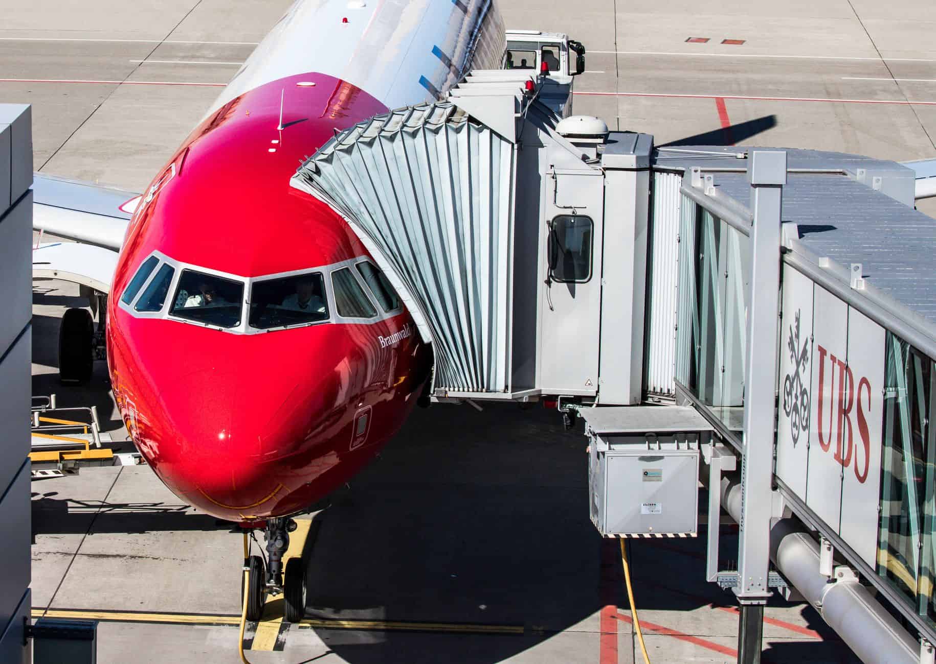 Red Airbus A320 aircraft at Zurich Airport terminal gate with boarding bridge attached.