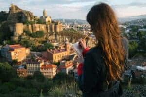 Woman writing in journal with a historic city view in the background, capturing inspiration from a stunning cityscape.