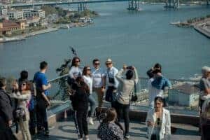 Group of tourists taking photos at a city overlook with a river and bridge in the background.
