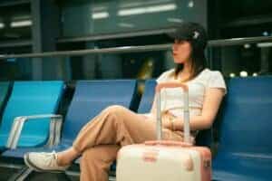 Young woman sitting at an airport terminal with luggage, looking thoughtful and waiting for her flight.