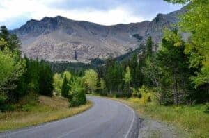 A winding road surrounded by lush trees leads to a stunning mountain range, perfect for nature enthusiasts.