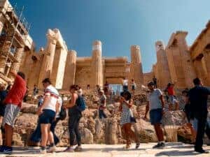 Crowds of tourists visiting the ancient Parthenon in Athens under a clear summer sky.